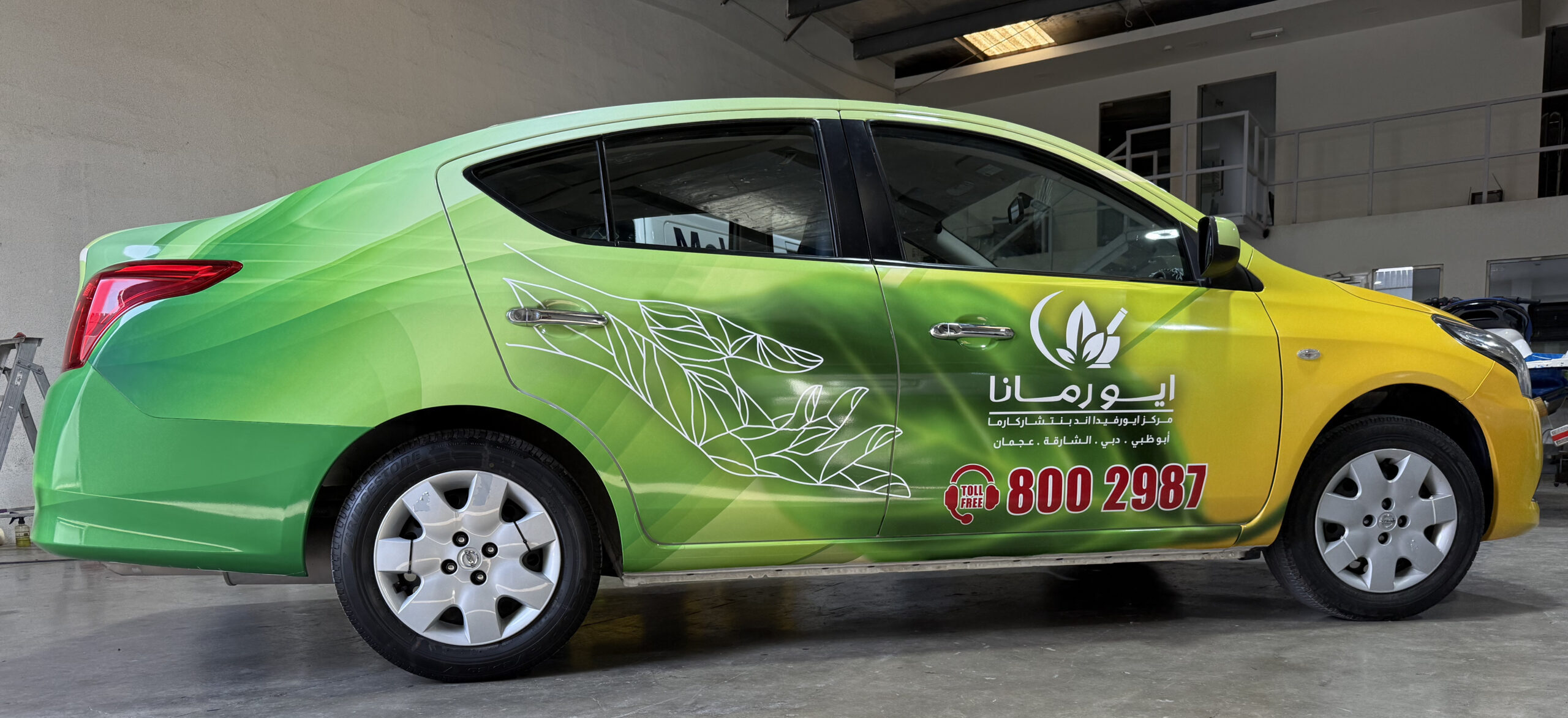 Green and yellow branded sedan with custom vinyl vehicle wrap inside Dubai car branding workshop for corporate mobile advertising-2