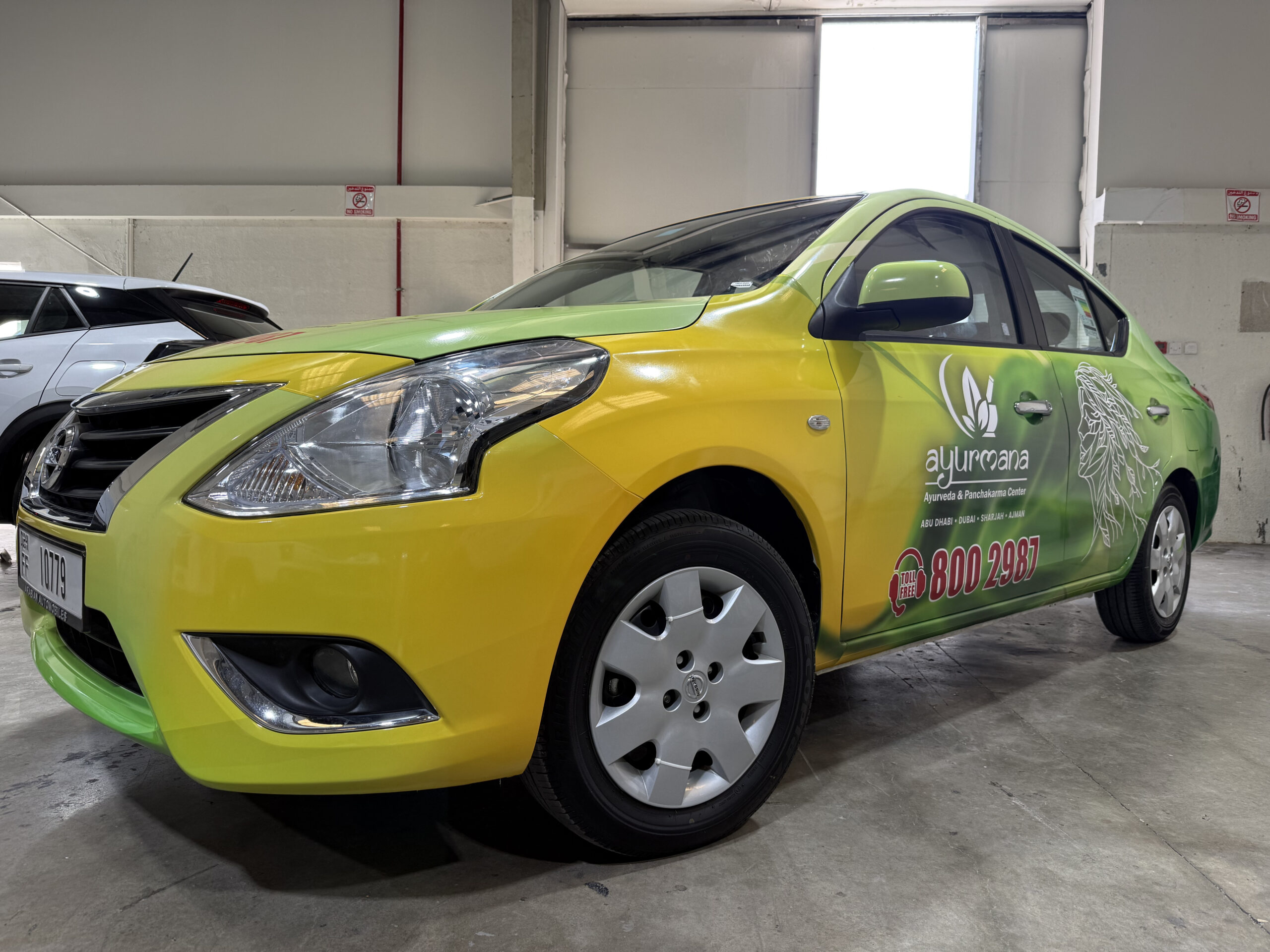 Green and yellow branded sedan with custom vinyl vehicle wrap inside Dubai car branding workshop for corporate mobile advertising-3